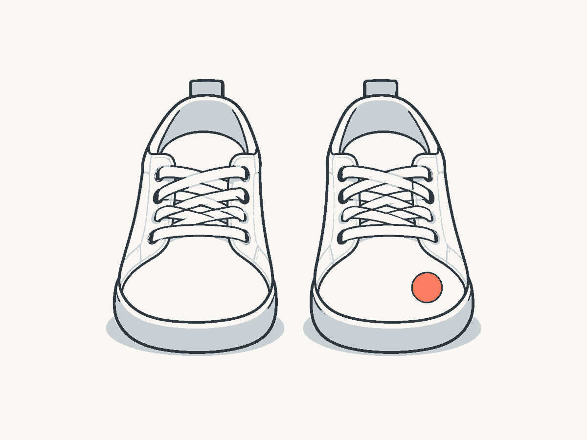 Zwei gleiche Schuhe nebeneinander: der linke schlicht, der rechte mit einem kleinen runden Aufkleber.